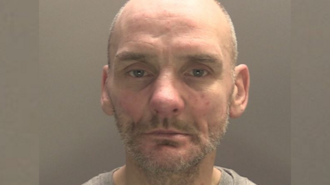 A mugshot of John David Sarwanskyj. He is bald, and has a short beard.