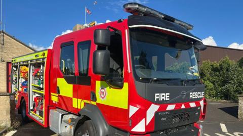 A Devon and Somerset fire engine parked outside a fire station on a sunny day.