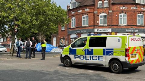 Four men standing near a police cordon on Reedswood Lane with a police van a short distance away