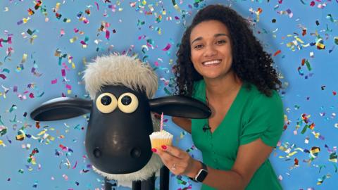 Nina holds a cupcake in front of Shaun the Sheep. The background is blue with confetti