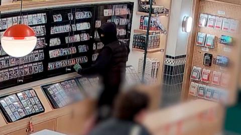 Hooded person dressed in all-black smashes glass display at Pokémon store