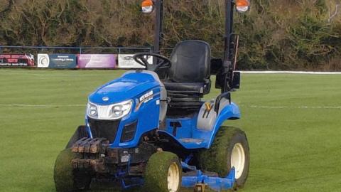 A picture of one of the tractors that has been stolen. This one was at Bude. It is blue in color with it traveling over a large area of grass.