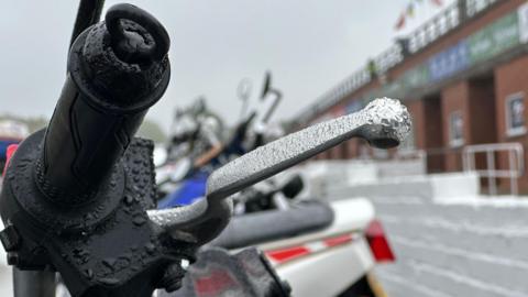 Rain on the handlebars of a motorcycle parked at the grandstand.