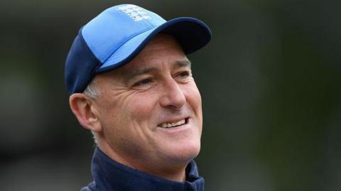 Graham Thorpe wearing a blue baseball cap and blue training top, pictured outdoors with a blurred green background.