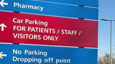 Large sign outside Ross-on-Wye Community Hospital. The red and blue sign has white arrows pointing to various places at the site.