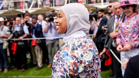 A female jockey wearing a hijab and top with colourful butterflies on it. 