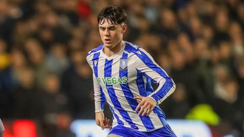 George Brown has a determined look on his face with his brow furrowed with his gaze towards the floor. He is running. He wears a blue and white vertically striped Sheffield Wednesday shirt.