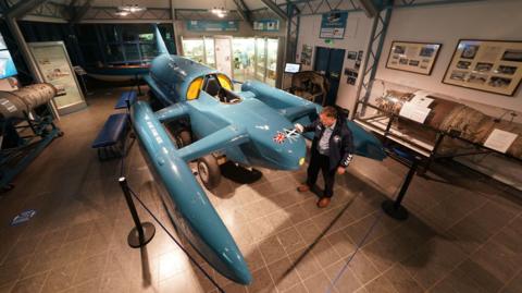 Bluebird, a jet-powered hydroplane, on display at Coniston's Ruskin Museum. Local businessman Phil Johnston is polishing the craft's nose. Two jet engines are on show nearby as well as several items of memorabilia relating to the Campbell family.