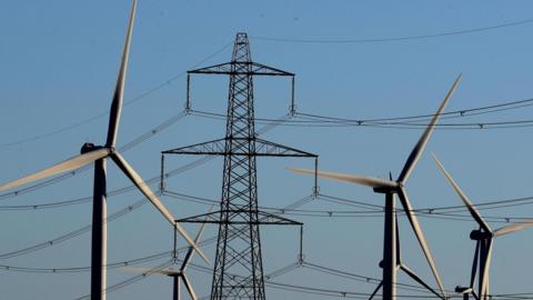 Wind turbines with an electricity pylon against a clear blue sky