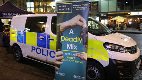 A police van and a Deadly Mix banner in a town centre in the evening. 