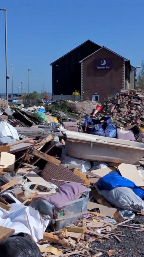 A view of a heap of rubbish left in Glastonbury. There is a bathtub and planks of wood.