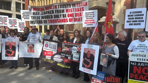 Bereaved families gathering outside the Lampard Inquiry at Arundel House, London. They are holding a variety of banners and photographs of their loved ones who they have lost. The slogans include sentences such as "if lessons were learned there would only have been one death". Some of the family members are wearing white T-shirts with "truth, justice, accountability" written on them.