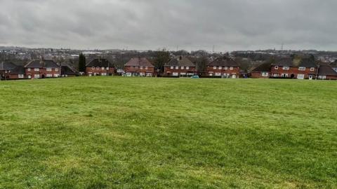 A row of semi-detached houses can be seen with a large open space in front of them.