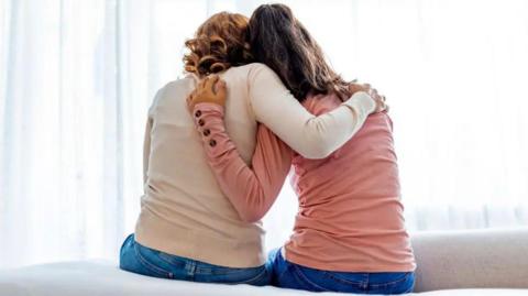 An anonymous woman hugging an anonymous teenage girl - both seen from behind