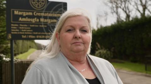 Katherine James, dressed in a grey cardigan, standing at the entrance to Margam Crematorium