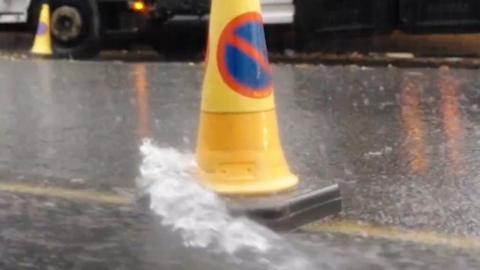 Rain splashing on to a traffic cone in a road. There is a tow truck in the background