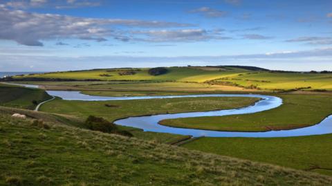 A meandering river within a sweeping green landscape. It looks picturesque. 