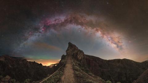 The arc of the Milky Way appearing over a rocky hill on Madeira. 
