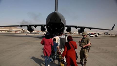 A member of British armed forces alongside Afghans boarding a plane at Kabul Airport in August 2021