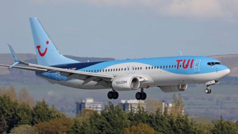 A Boeing 737 flying in the sky with a light blue, dark blue and white TUI livery