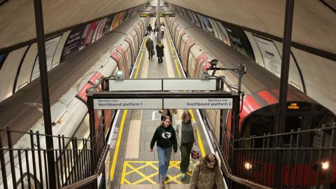 Clapham Common Tube station shows two trains either side of the platform with passengers walking along it 