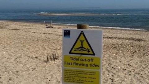 A sandy beach with a warning sign on wooden post and sea behind.