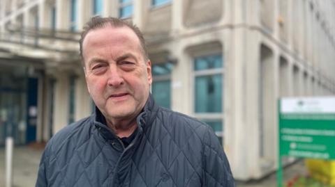 Phil Bialyk wearing a quilted navy blue jacket in front of the Exeter City Council offices