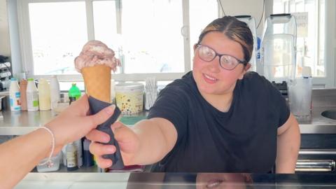 Woman in ice cream shop hands over a cone to a customer