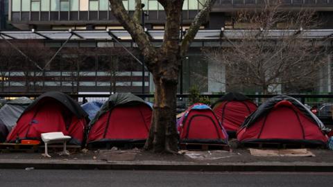 Red tents line a central London street beneath a bare tree. 