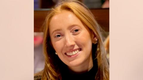 Close up of Chloe Moffat, who has long red hair, smiling at a camera.