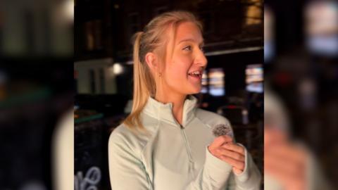A woman with blonde hair in a white running top in a dark city street.