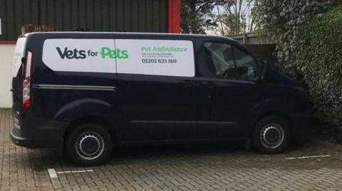 Dark blue van with pet ambulance branding parking outside a building.