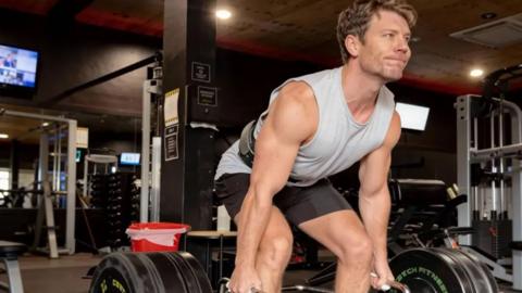 Dr Michael Mrozinski lifting two kettlebells inside a gym.