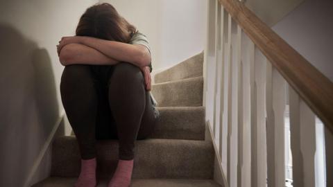 An upset woman sitting on some stairs with her head in her knees