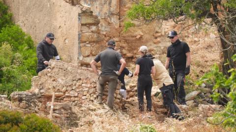 Members of a search team, wearing dark clothes and baseball caps, look through a derelict property 