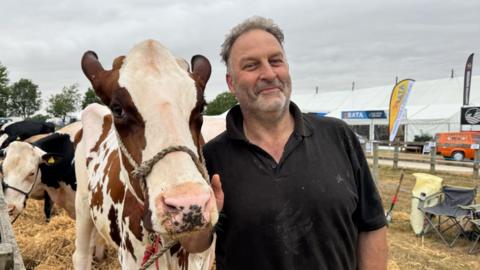 Man wearing a black polo top standing next to a cow at a farm show