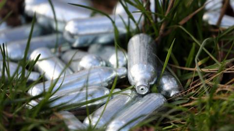 A pile of small, silver canisters of nitrous oxide, or laughing gas, discarded on a patch of grass.