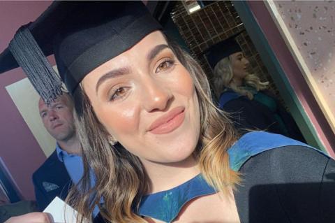 Sophie Morgan wears a black university cap and gown and smiles at the camera. She has brown short hair and brown eyes. 
