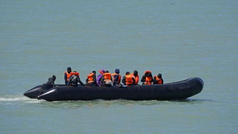 A large rubber rib boat with several men on board wearing orange life jackets out at sea.