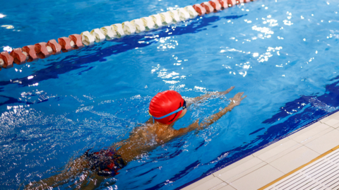 A child wearing goggles and an orange swim hat in the swimming pool in a breast stroke motion.