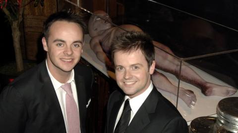 Ant and Dec wear black suits while standing in front of a model of an alien in a glass box