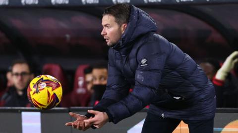 Tom Cleverley goes to catch a ball while standing on the touchline 