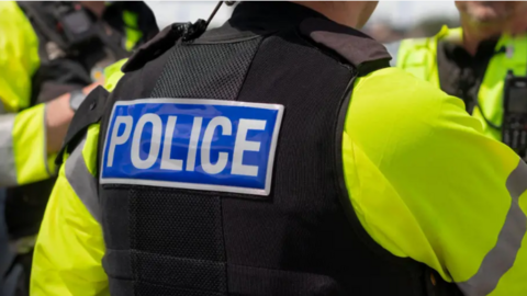 Shows police officers in flak jackets and yellow bibs