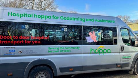 A bus with writing on the side. It reads: "Hospital hoppa for Godalming and Haslemere" and "Door to door hospital transport for you."