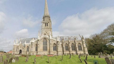 The church is an unusal shape. The bell tower and steeple are in the middle of the church which has an entrace at one end and large stained glass windows underneath the tower. 