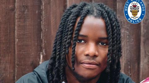 A close-up of a young man with dreadlocks who is looking at the camera. A West Midlands Police logo is in the top right-hand corner of the photo.