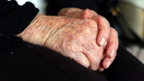 A close-up of an elderly person's hands clasped together on their lap.