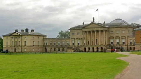Kedleston Hall, which is a stately home, behind a patch of grass and grey skies
