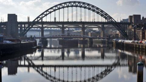 The Tyne Bridge connecting Newcastgle and Gateshead. The bridge's reflection can be seen in the water. The Swing Bridge can be seen underneath the Tyne Bridge.