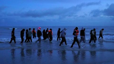 A group of migrants are seen at dawn wading through the shore in France to board a small boat